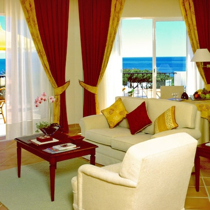 A living room with a sofa, armchairs, a coffee table, and a lamp. There is a view of the ocean through large windows.