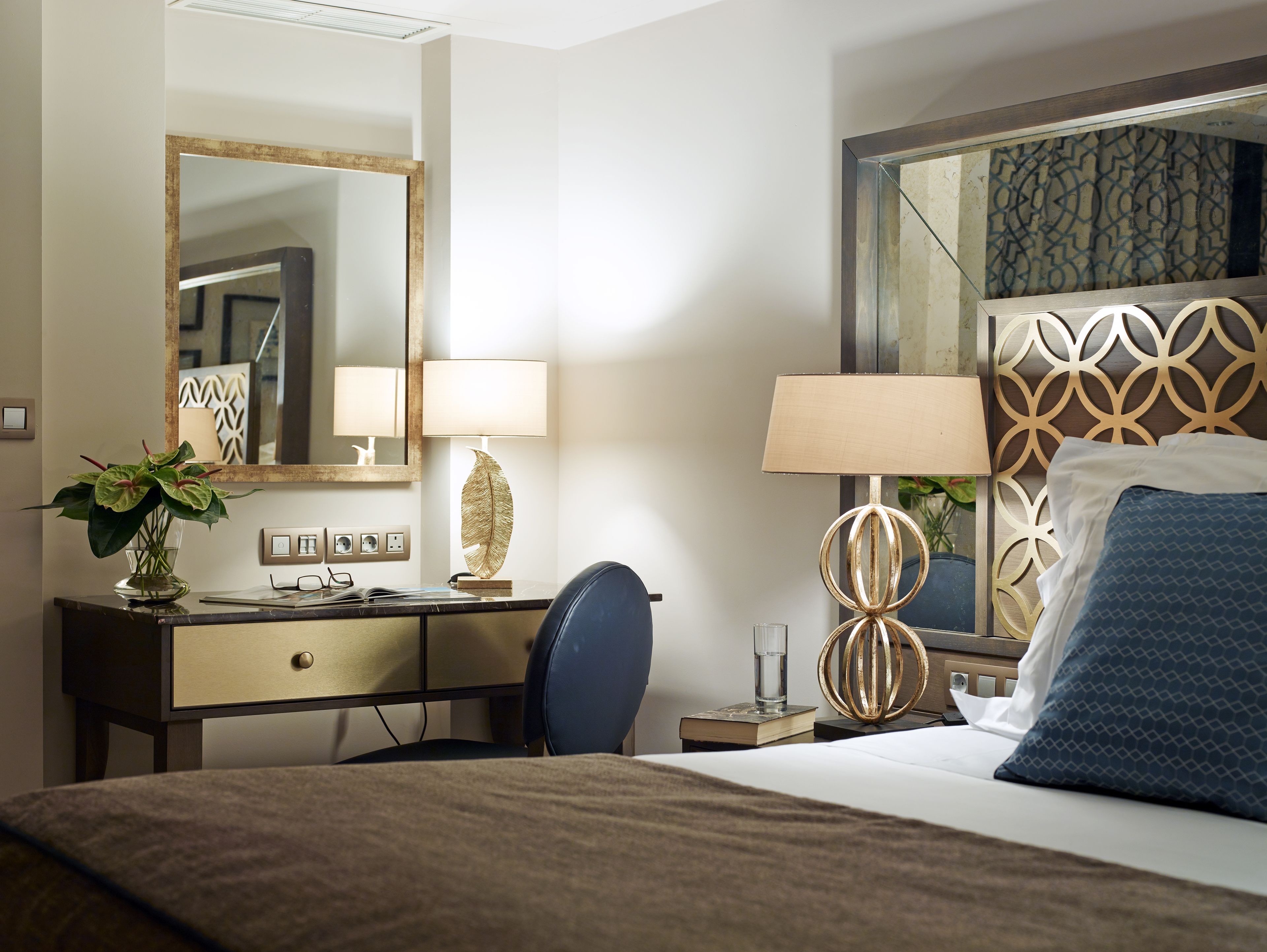 Une chambre d’hôtel avec un lit, un bureau doté d’une lampe, une chaise et un grand miroir.