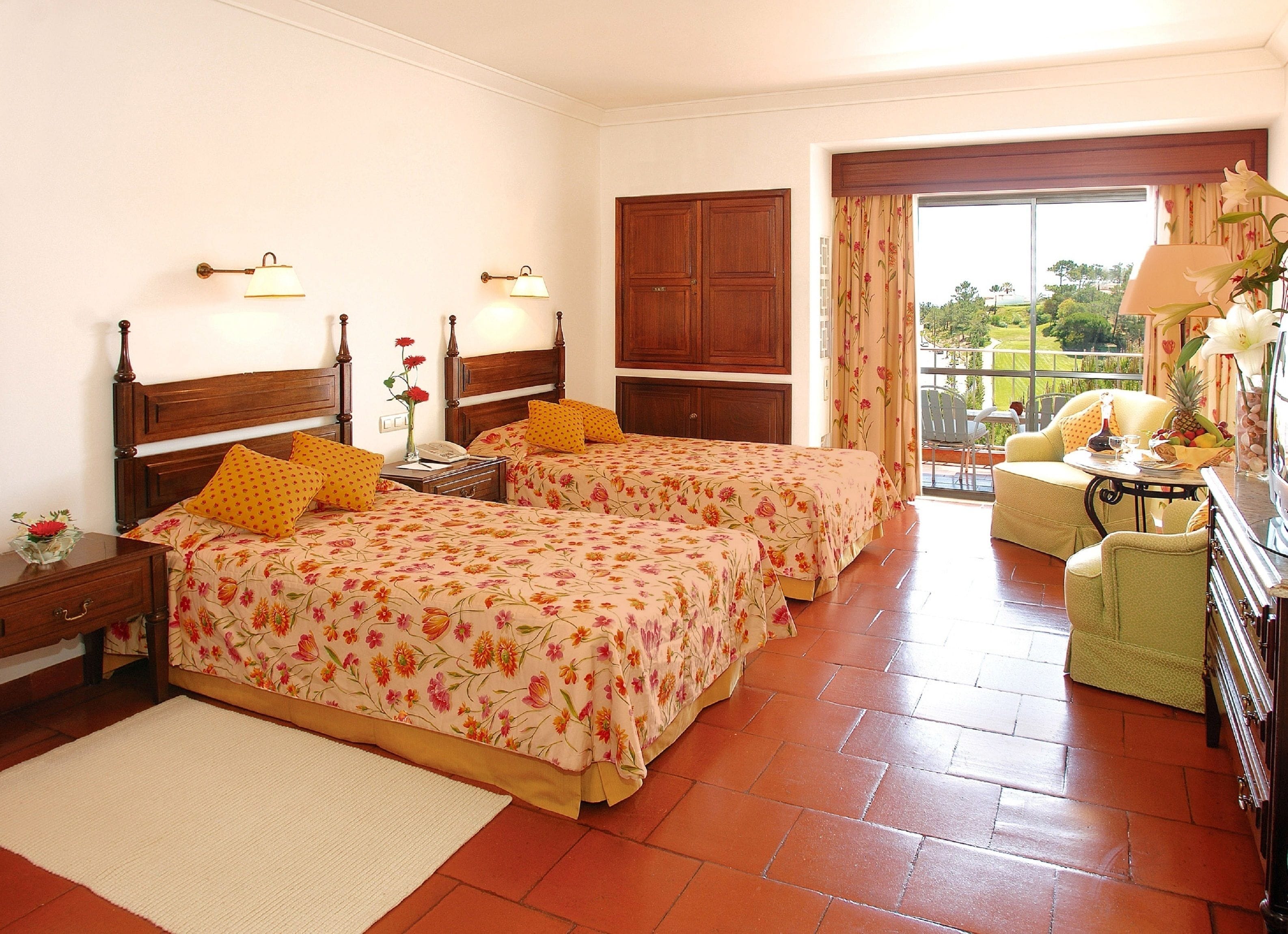 A hotel room with two beds, a sitting area with a table, and a view of the outdoors.