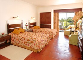 A hotel room with two beds, a sitting area with a table, and a view of the outdoors.