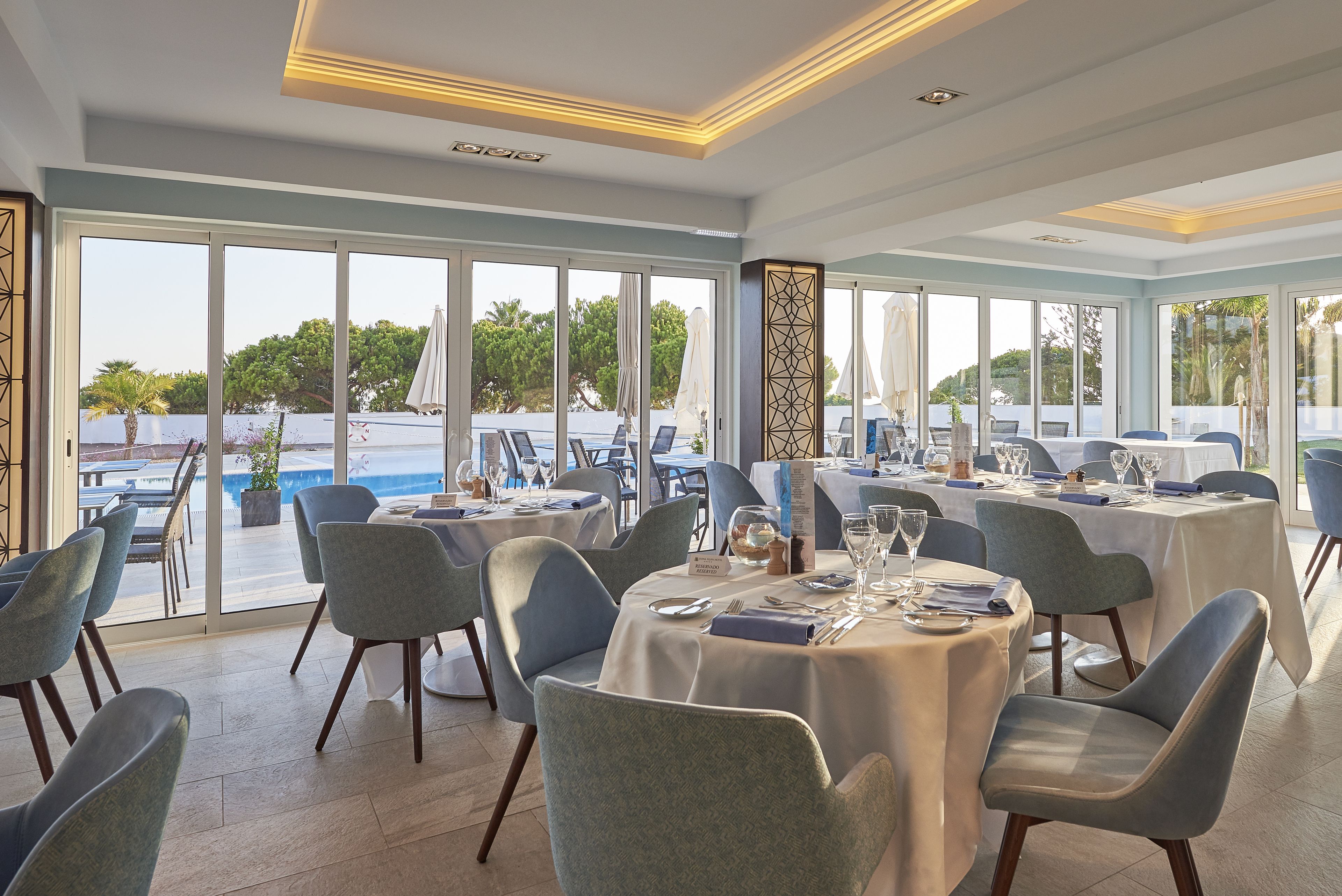 A dining area with round tables, chairs, and a pool view.