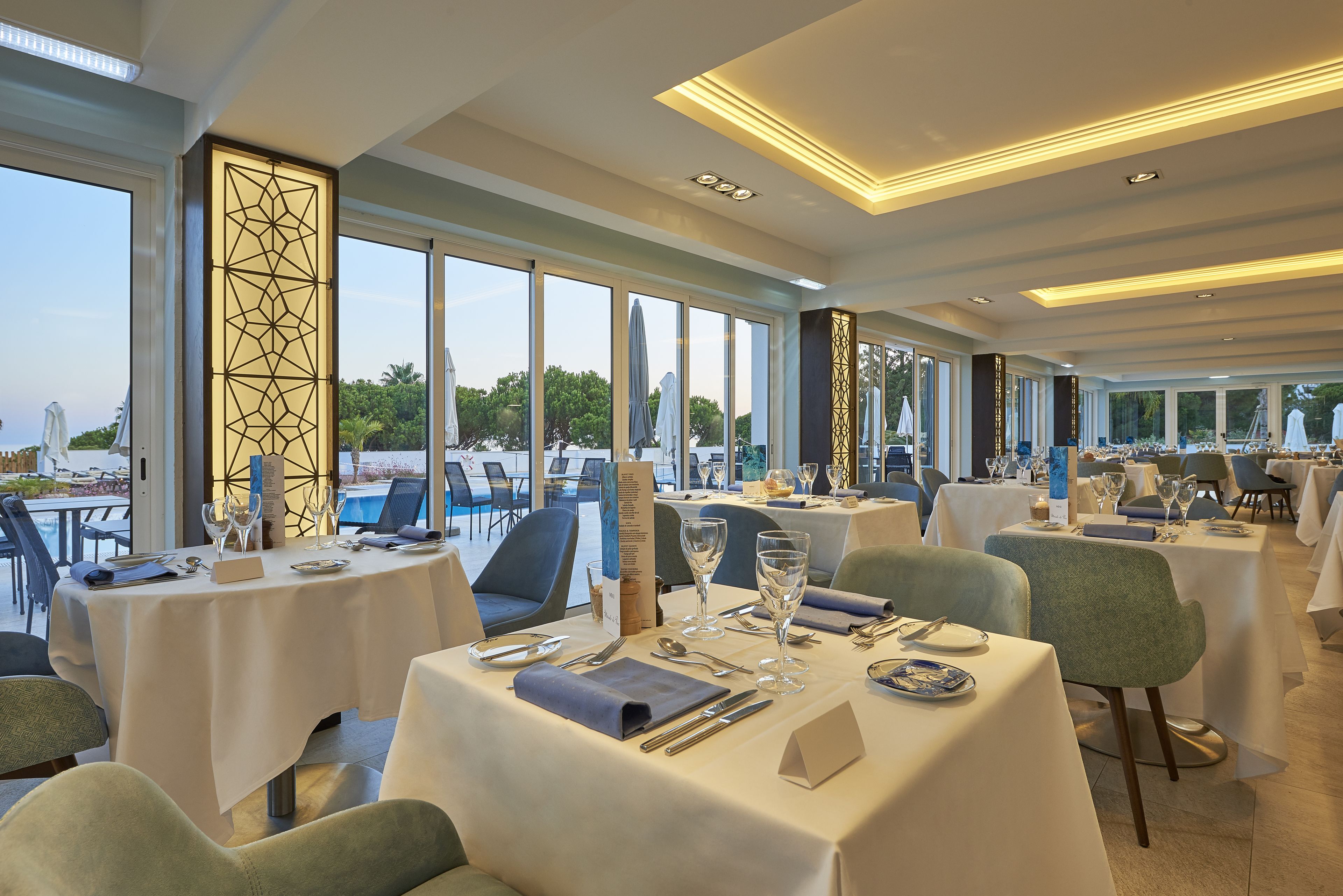 Ein Restaurant mit gedeckten Tischen, großen Fenstern und Blick ins Freie.