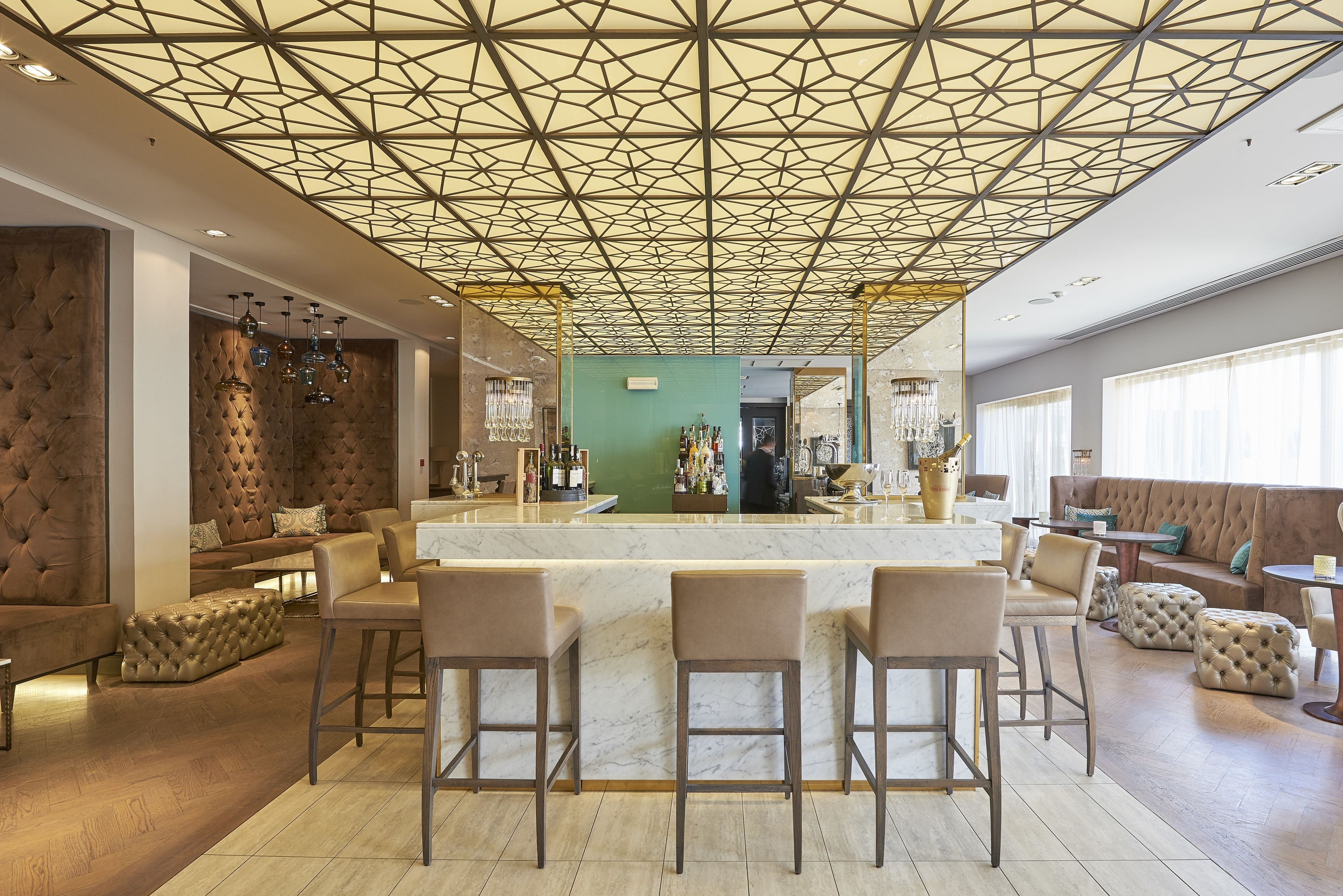 A modern bar area with a geometric ceiling design, plush seating, and a marble counter.