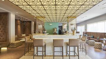 A modern bar area with a geometric ceiling design, plush seating, and a marble counter.