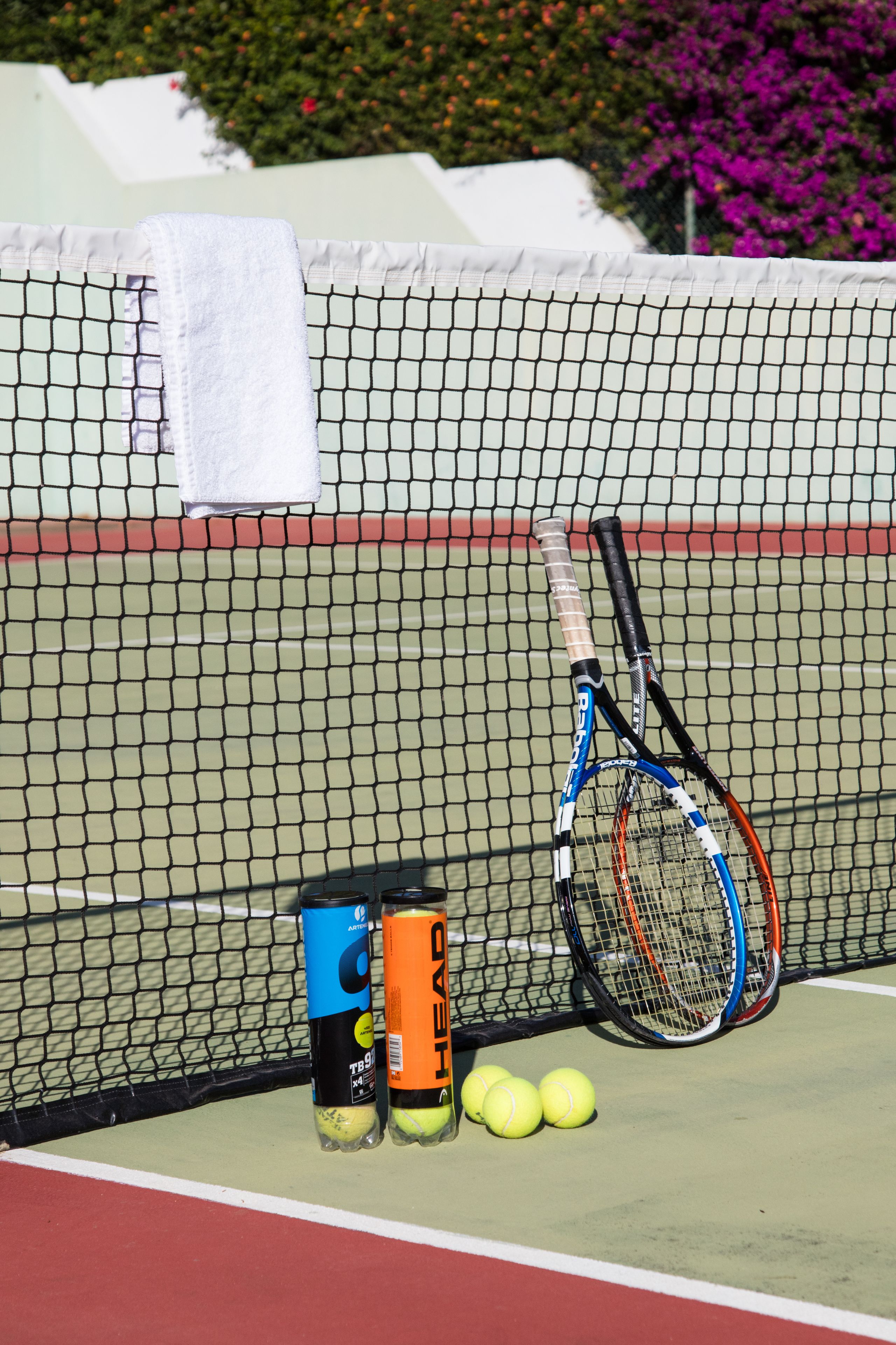 A tennis court with two tennis rackets, a towel, and two cans of energy drinks.