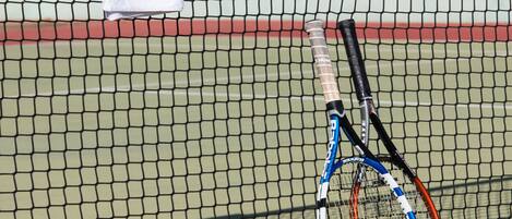 A tennis court with two tennis rackets, a towel, and two cans of energy drinks.