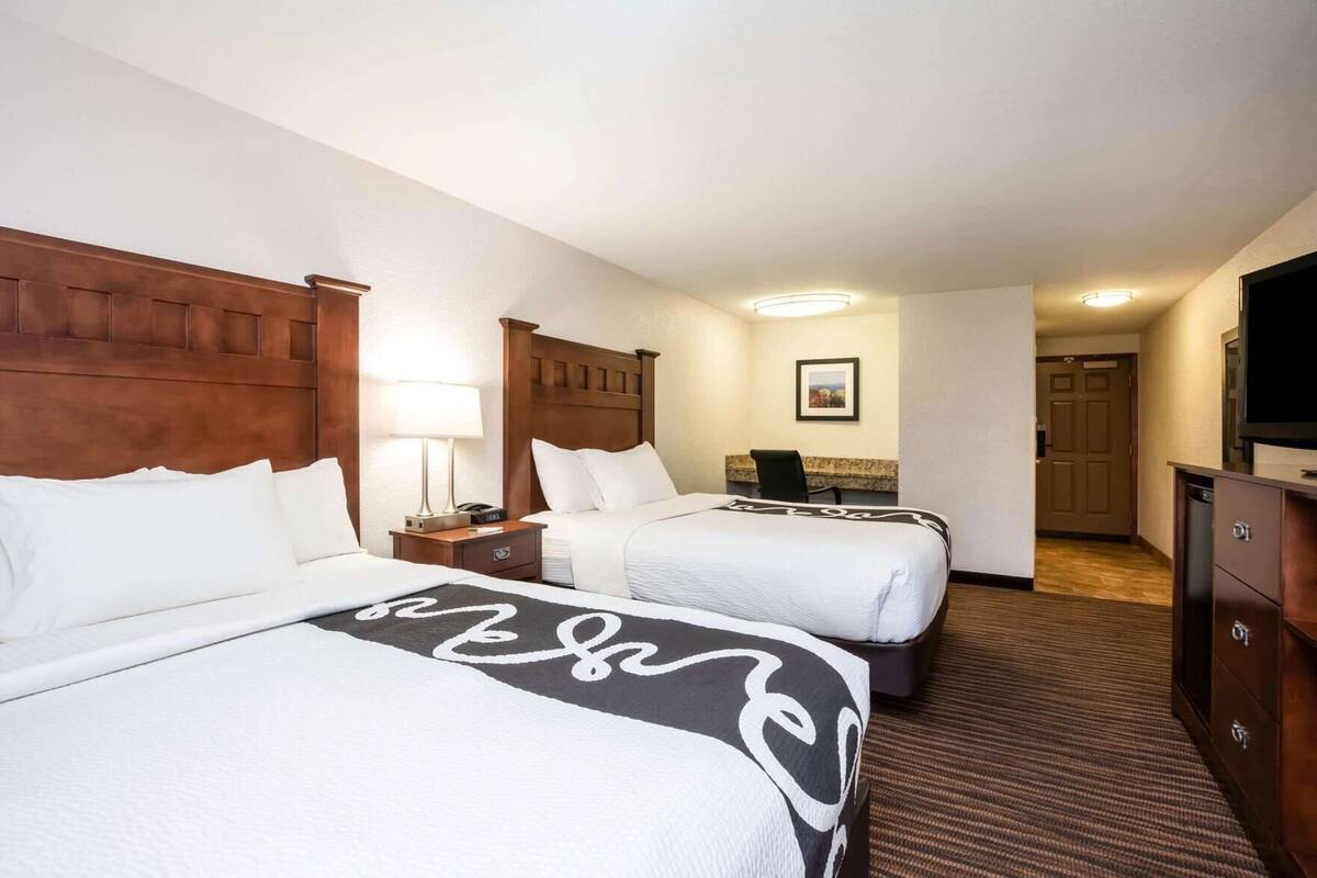 A hotel room with two beds, a desk, a chair, a television, and a framed picture on the wall.