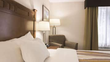 Habitación de hotel con una cama grande, una silla, un escritorio con lámpara y una ventana con cortinas.