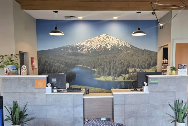 Un comptoir d’accueil orné d’une grande fresque représentant une montagne et un lac, deux lampes suspendues et un écran Samsung.