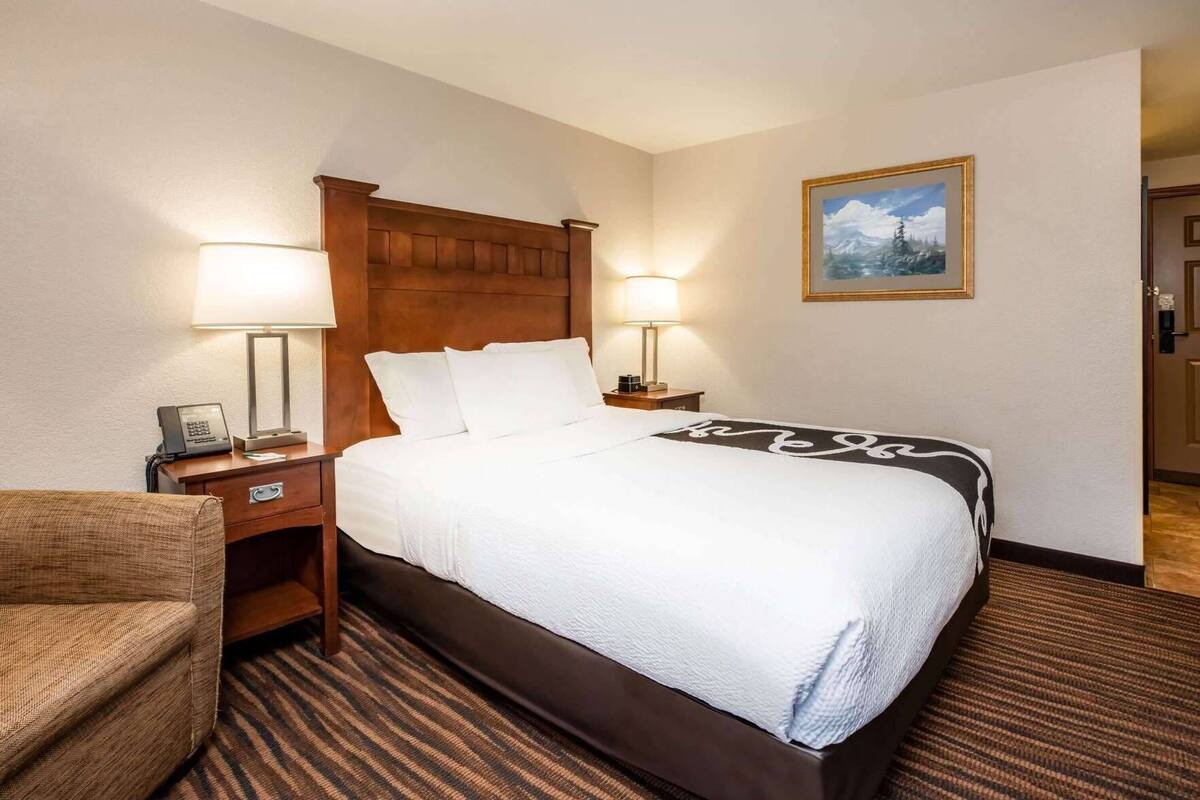 A hotel room with a large bed, two bedside tables with lamps, a chair, and a painting on the wall.