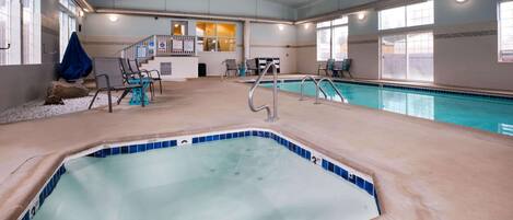 An indoor swimming pool with a hot tub, seating area, and a reception desk.