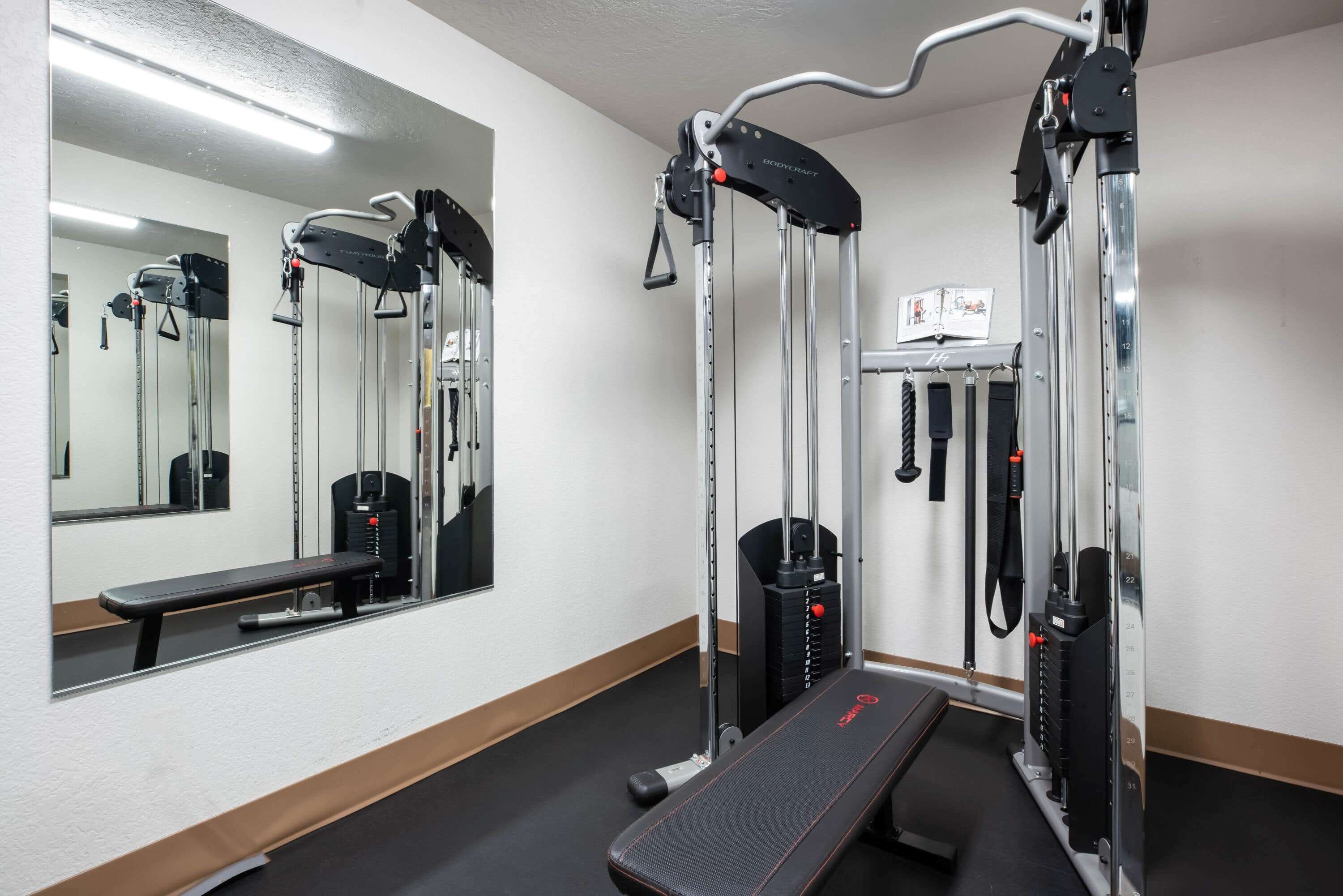 Un gimnasio con equipo de ejercicio, una banca y un espejo.