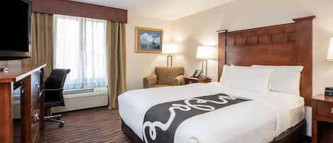 A hotel room with a large bed, a desk with a TV, a chair, two bedside lamps, and a painting on the wall.