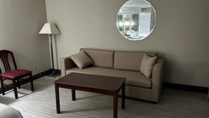 Ein Zimmer mit einer Couch, einem Holztisch, einem roten Sessel, einer Stehlampe und einem runden Spiegel an der Wand.