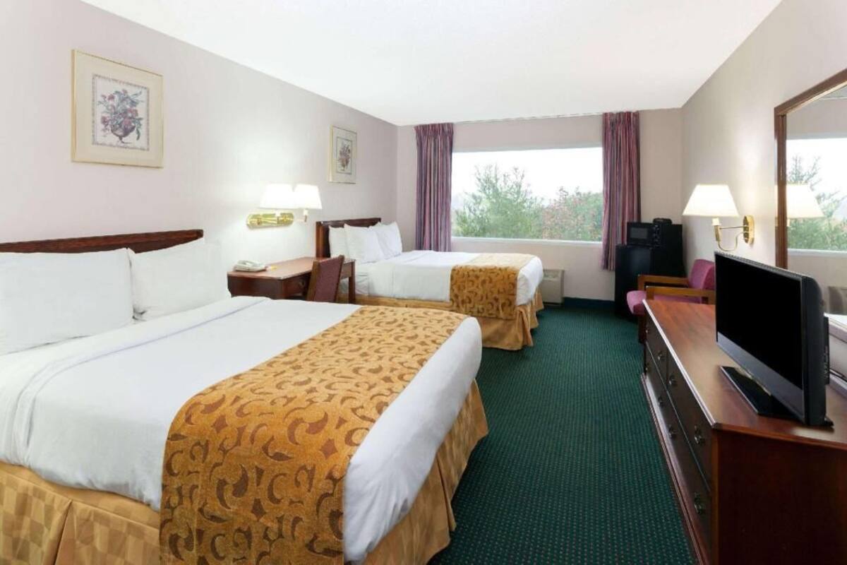 A hotel room with two beds, a TV, a desk, and a window with curtains.