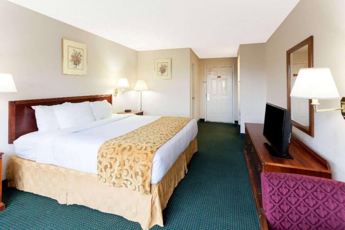 A hotel room with a bed, two bedside lamps, a television, and a door leading to another room.