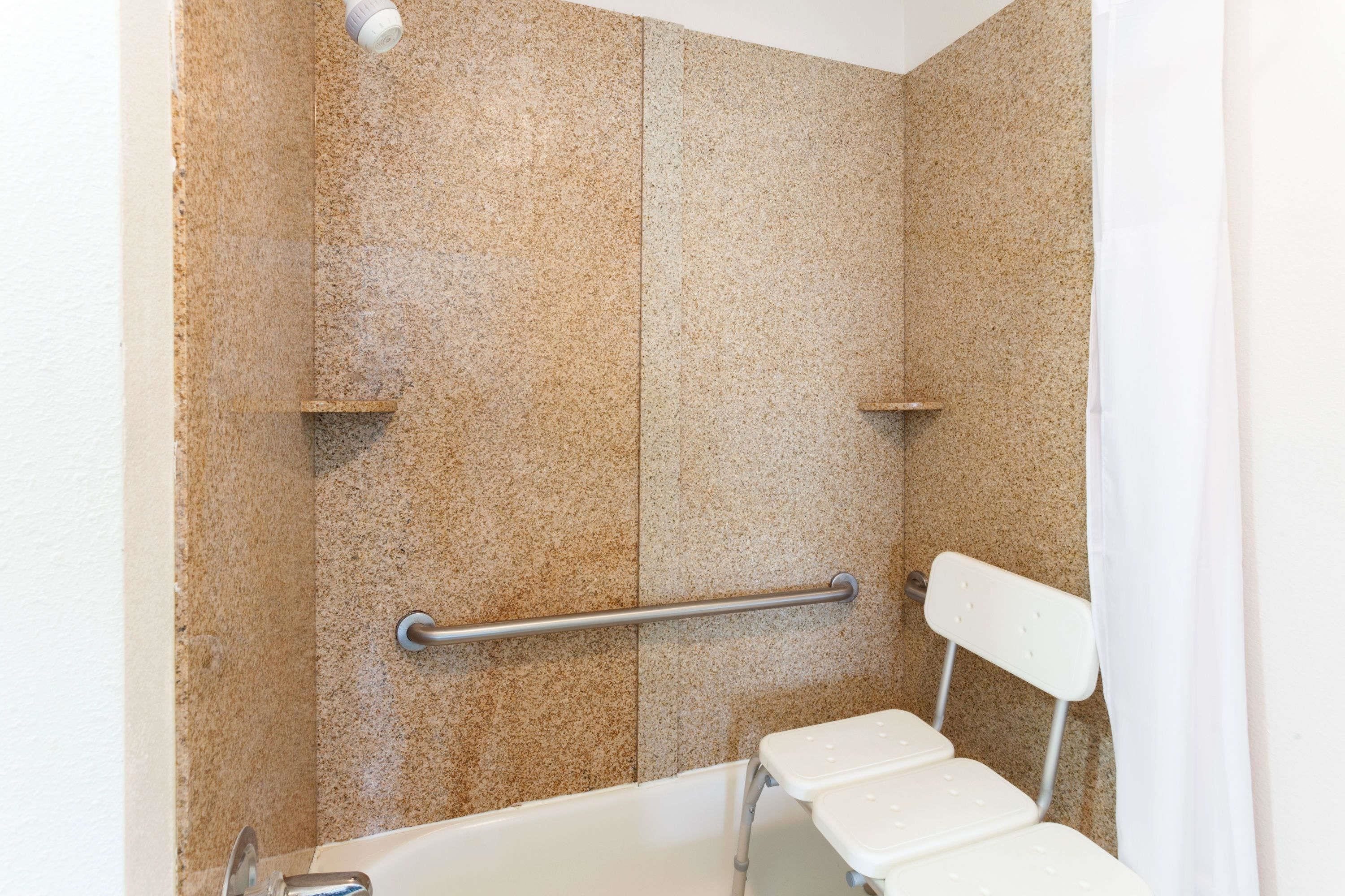 A bathroom with a shower area, grab bars, and a white bathtub.