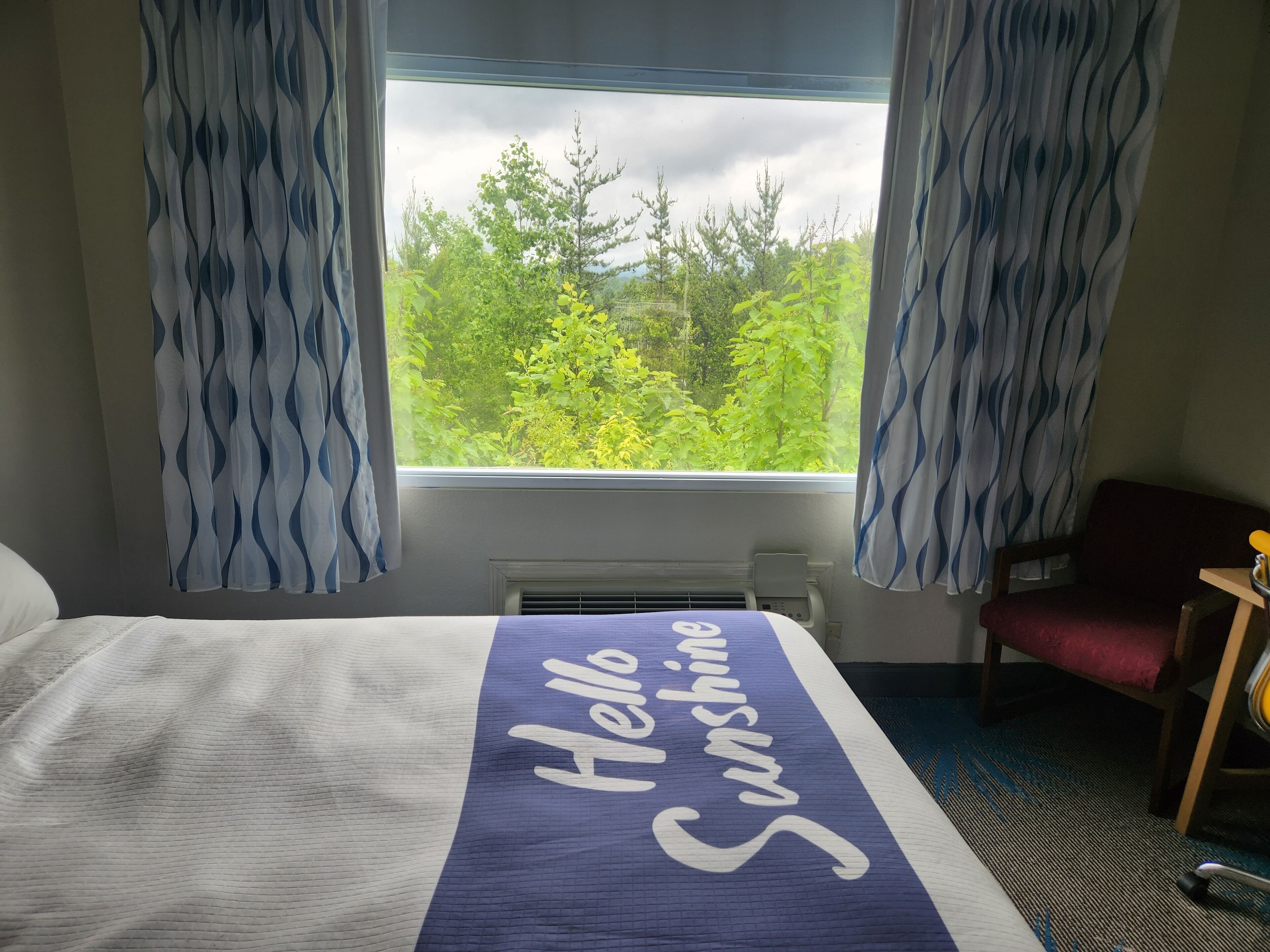 Ein Hotelzimmer mit einem Bett, einem Sessel und einem Fenster mit Vorhängen.