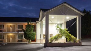 Ein Motel mit überdachtem Parkplatz, einem zweigeschossigen Gebäude und einem gut beleuchteten Eingang.