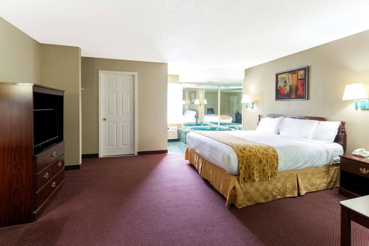 A hotel room with a bed, a television, a desk, and a bathroom visible through an open door.