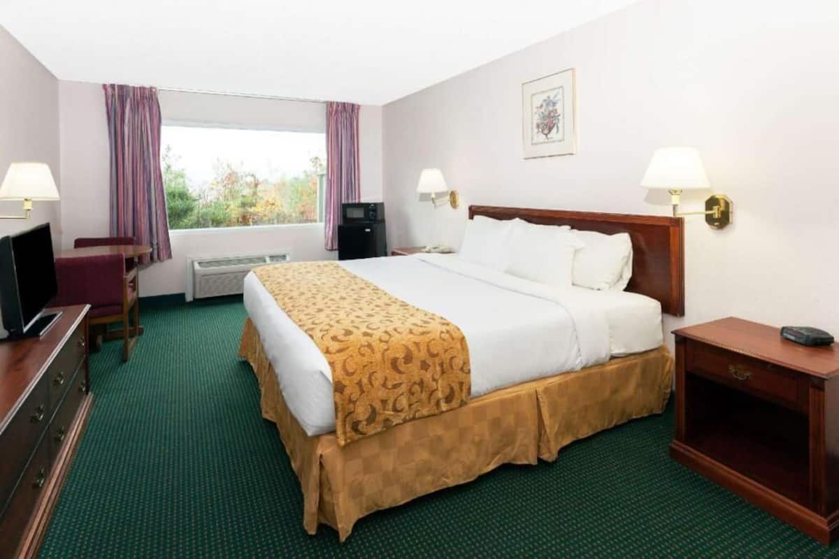 A hotel room with a bed, a desk, a chair, a television, a lamp, and a window with curtains.