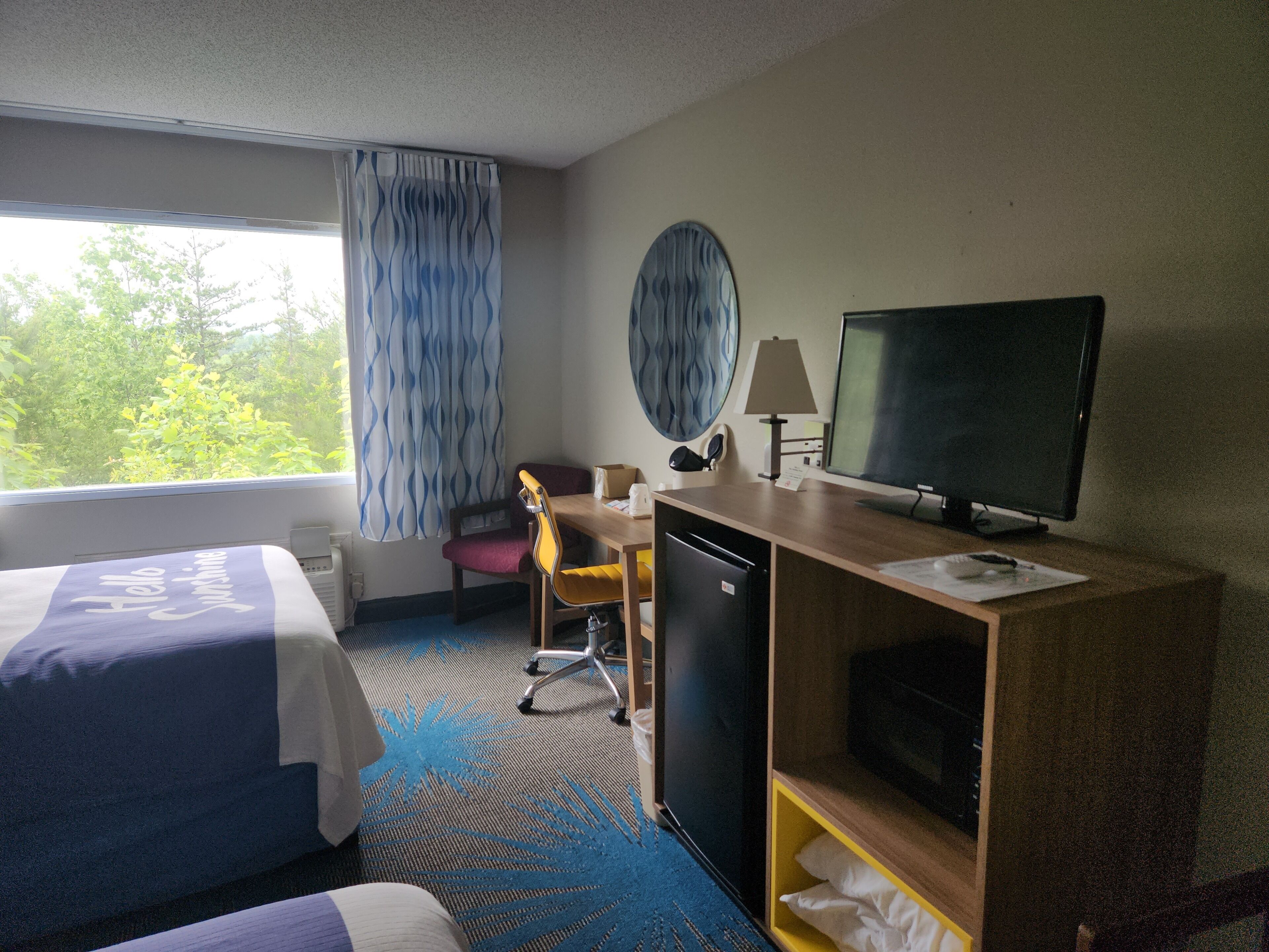 Une chambre d’hôtel avec deux lits, un bureau avec un ordinateur, une télévision et un petit réfrigérateur.