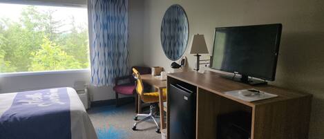 Une chambre d’hôtel avec deux lits, un bureau avec un ordinateur, une télévision et un petit réfrigérateur.