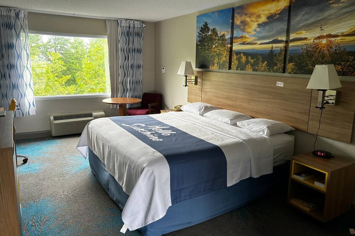 A hotel room with a bed, a desk, a chair, a small table, and a window with curtains.