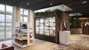 A modern hotel lobby with a beverage refrigerator stocked with drinks, a coffee machine, and a variety of snacks. - NH Frankfurt Airport (Kelsterbach)