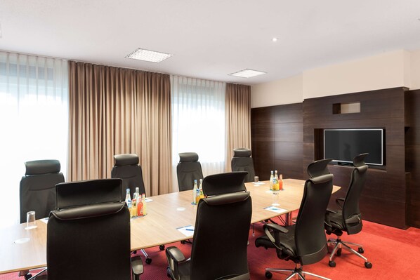 A conference room with a long table, six black chairs, a flat-screen TV, and a red carpet.