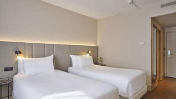 Ett hotellrum med två sängar, ett nattduksbord med en lampa, en väggmonterad lampa och en dörr som leder till ett annat rum.