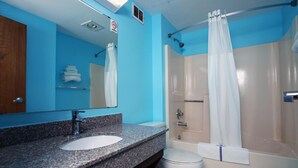 Ein Badezimmer mit blauer Wand, einer Granit-Arbeitsplatte, einem weißen Waschbecken, einer Toilette und einer Dusche mit weißem Vorhang.