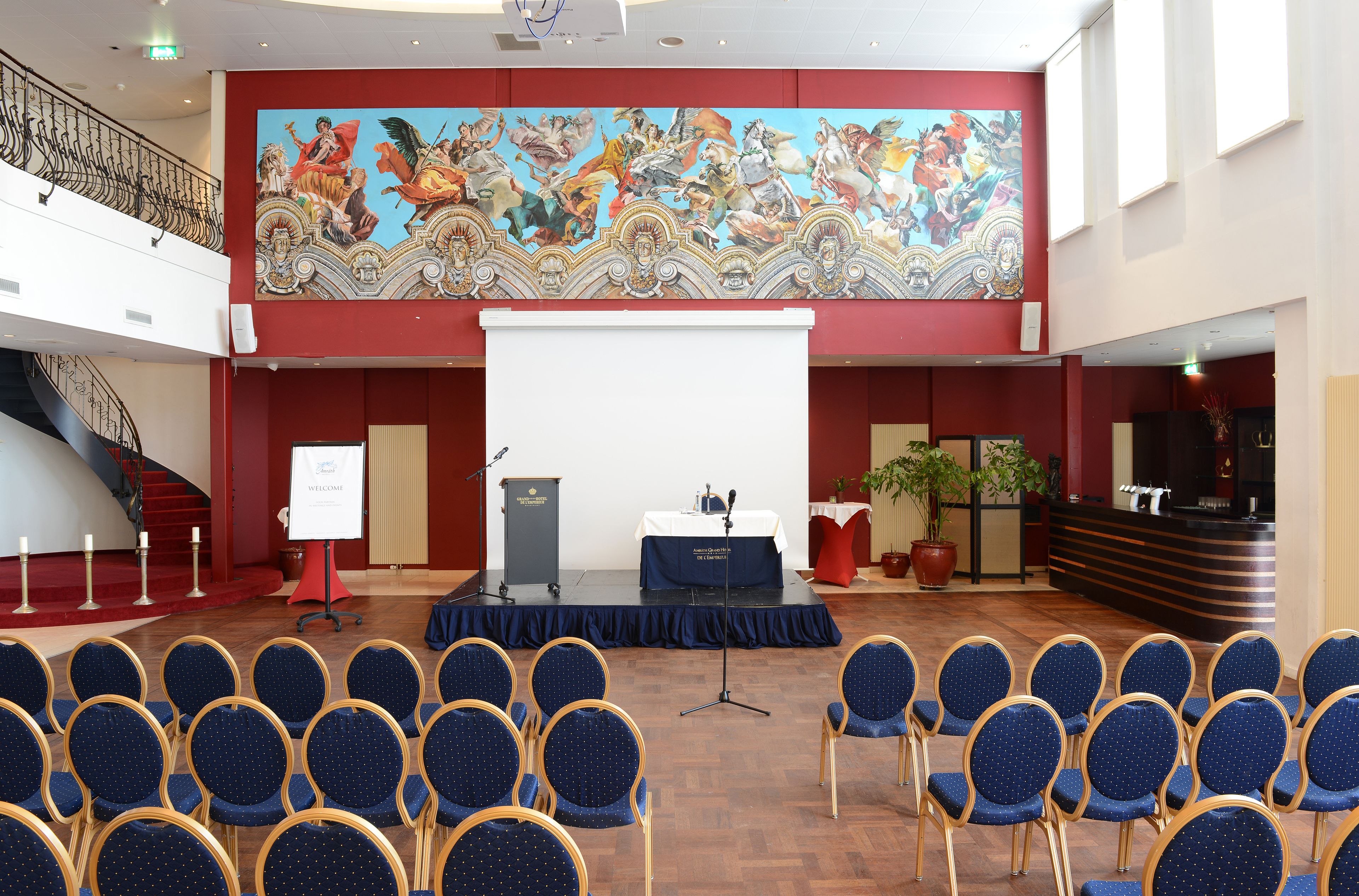 A conference room with a stage, a large mural, and rows of chairs.