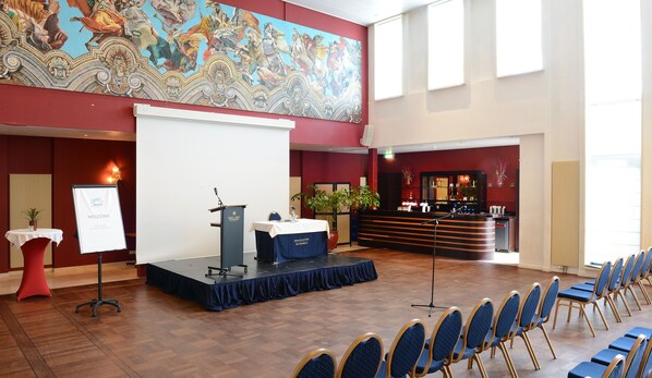 Un salón de conferencias con un escenario, una mesa de recepción y filas de sillas.