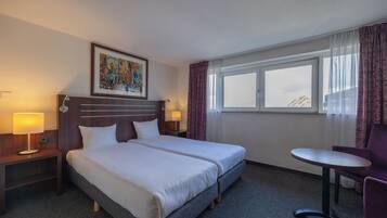 A hotel room with a double bed, two bedside tables with lamps, a small round table, and a chair.