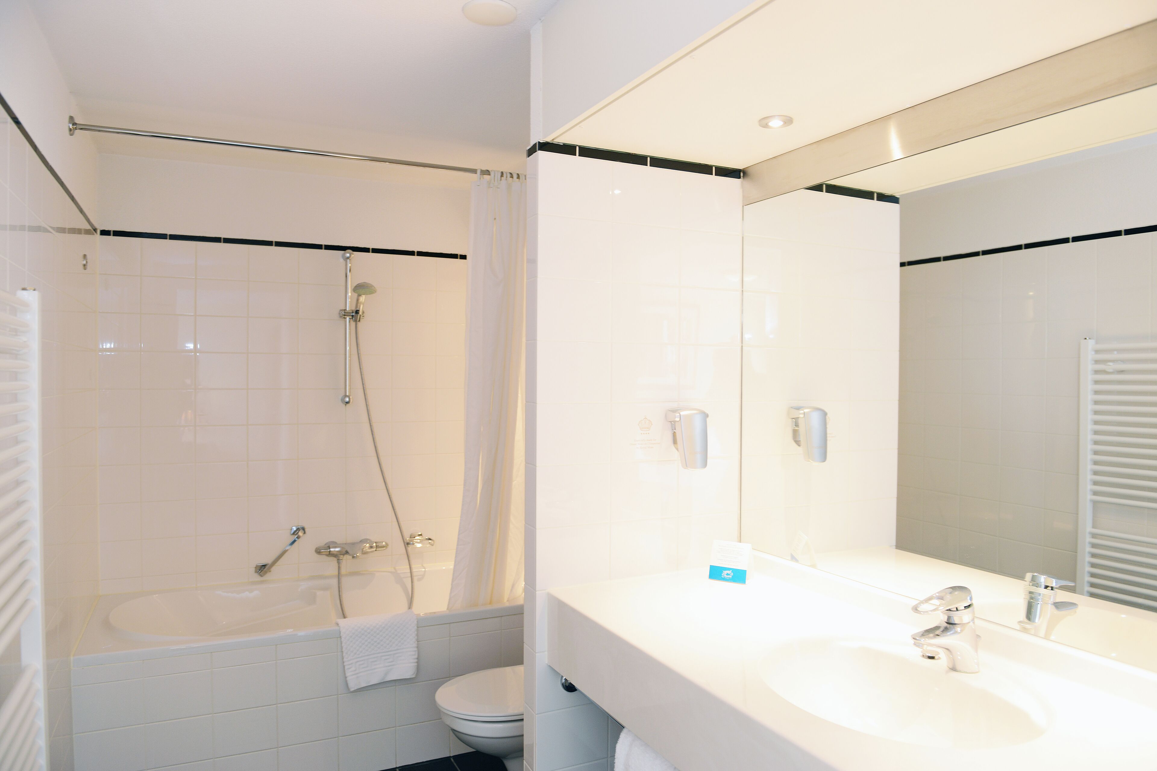 Un baño moderno con bañera, inodoro y un espejo grande sobre el lavamanos.