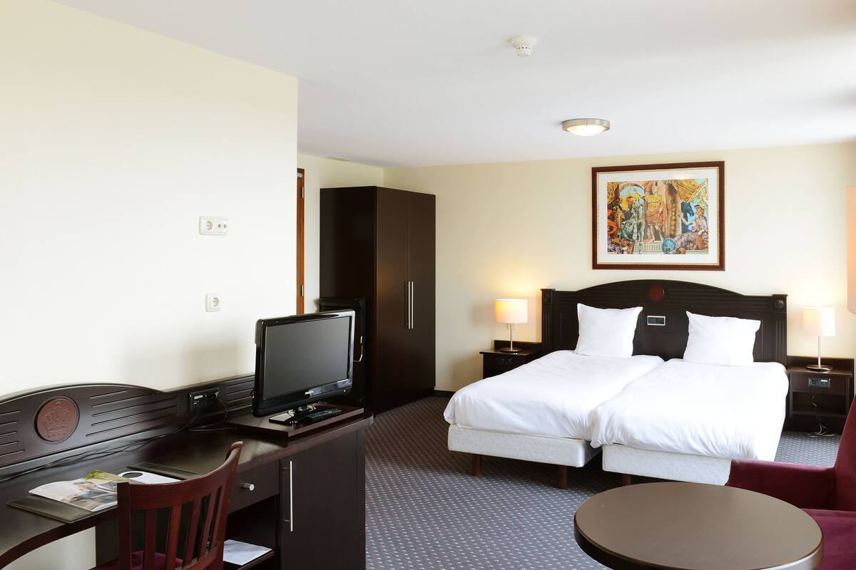 A hotel room with a bed, a desk with a computer, a chair, a TV, and a small table.
