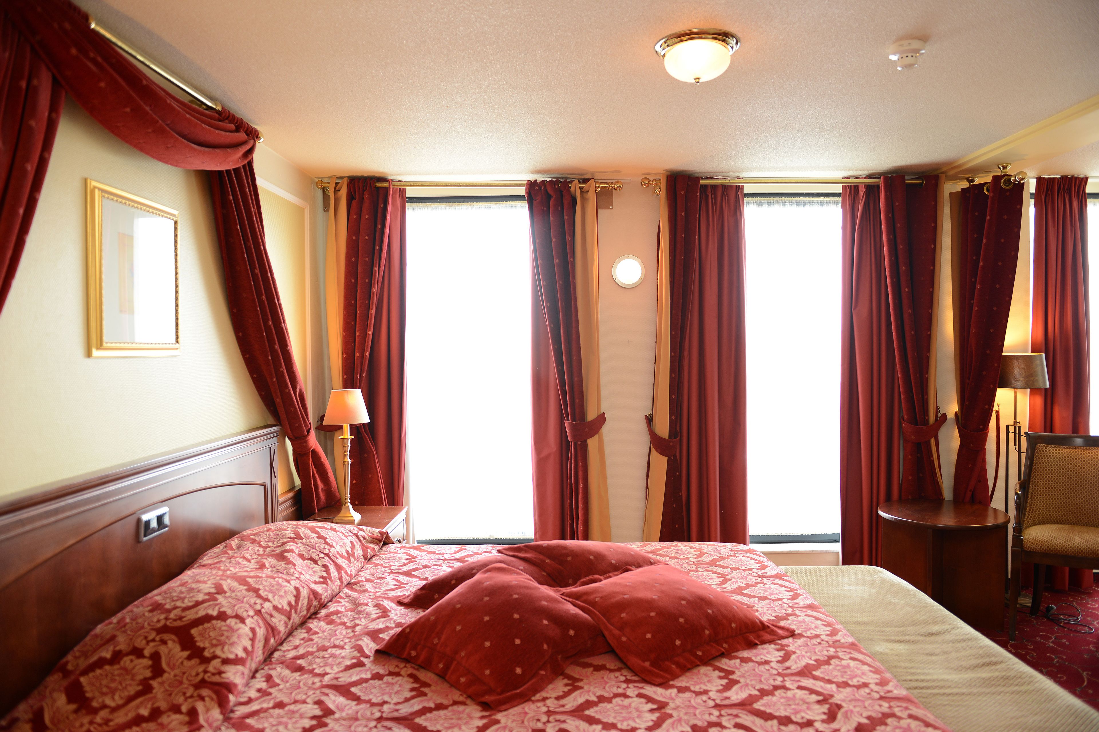 Een hotelkamer met een groot bed, een stoel, een lamp en uitzicht op het omliggende landschap door de ramen.