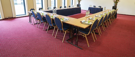 Un salón de conferencias con una larga mesa, sillas y una alfombra roja.