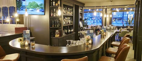 Zona de bar con mostrador, taburetes y estantes llenos de botellas, además de un televisor montado en la pared.