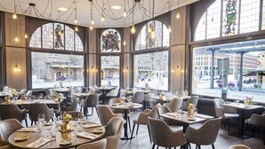 A restaurant with round tables, chairs, and large windows offering a view of the street. - Amrâth Grand Hotel de l'Empereur (Maastricht)