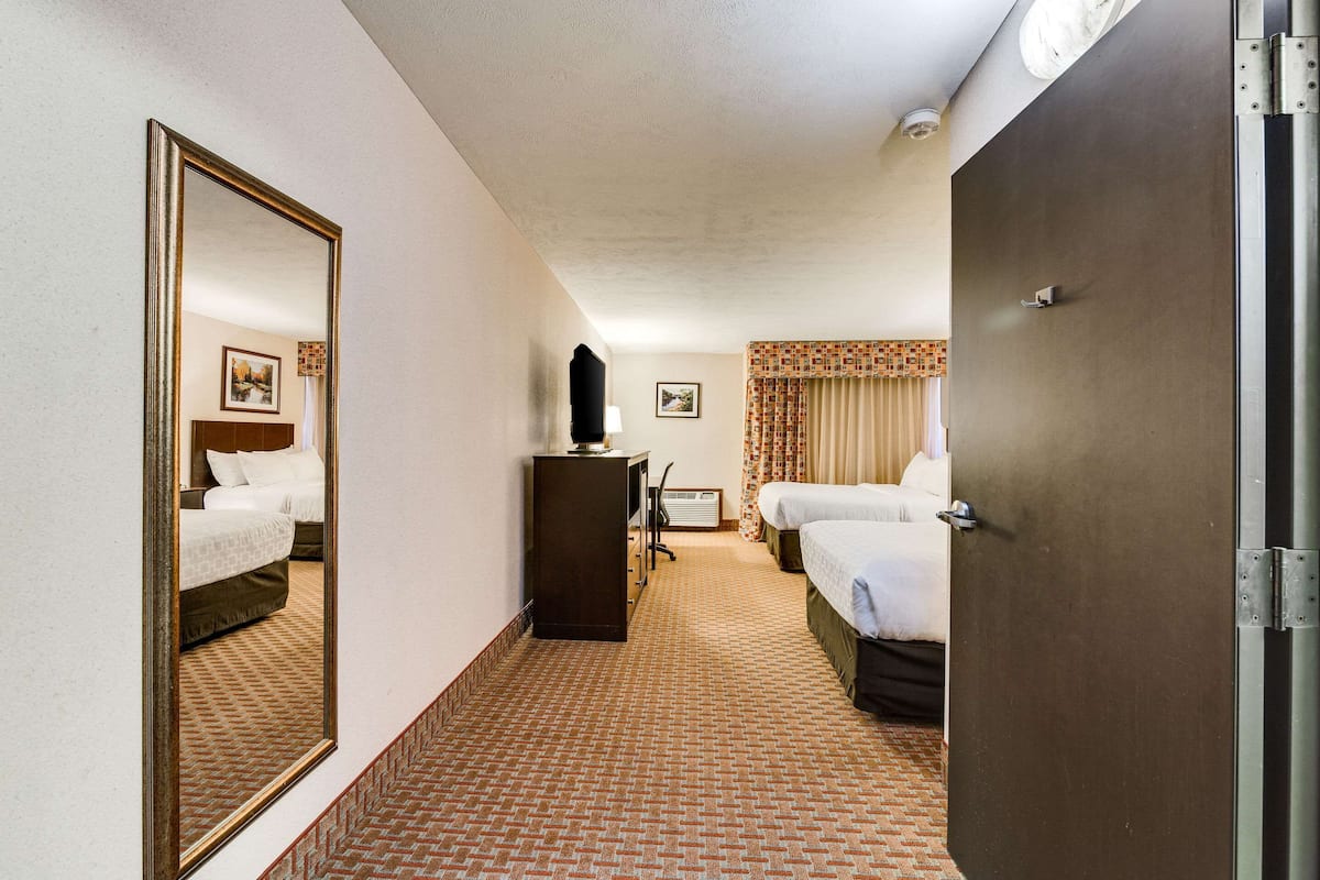 A hotel room with a large mirror, a desk with a lamp, two beds, and a door.
