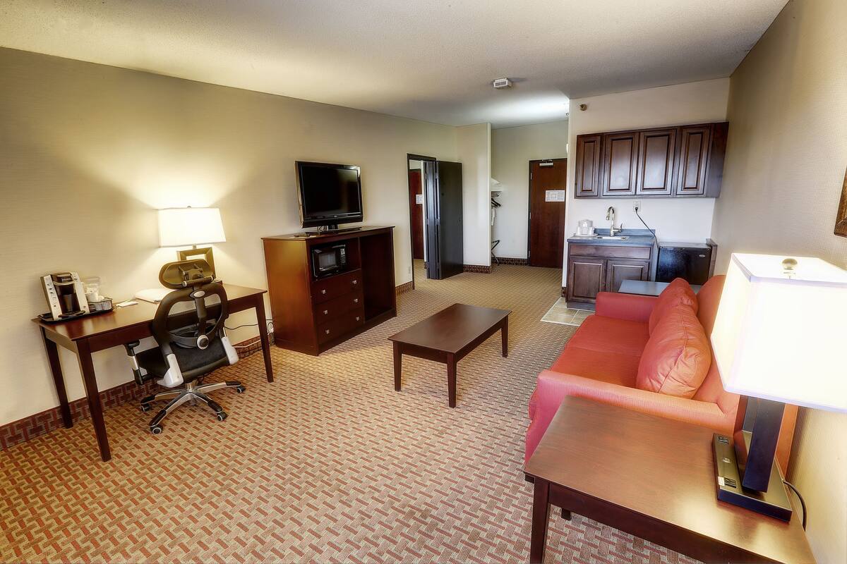 A hotel room with a desk, office chair, television, sofa, and a kitchenette area.