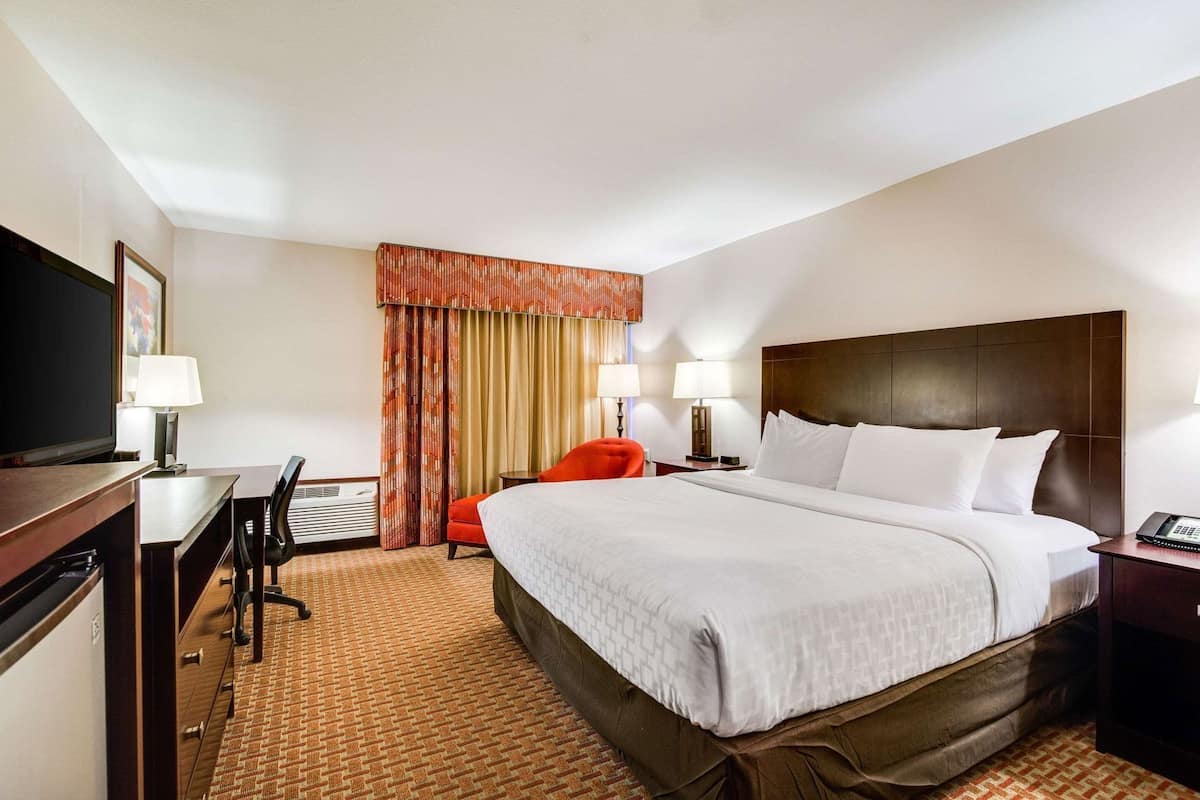 A hotel room with a bed, desk, chair, and a television.