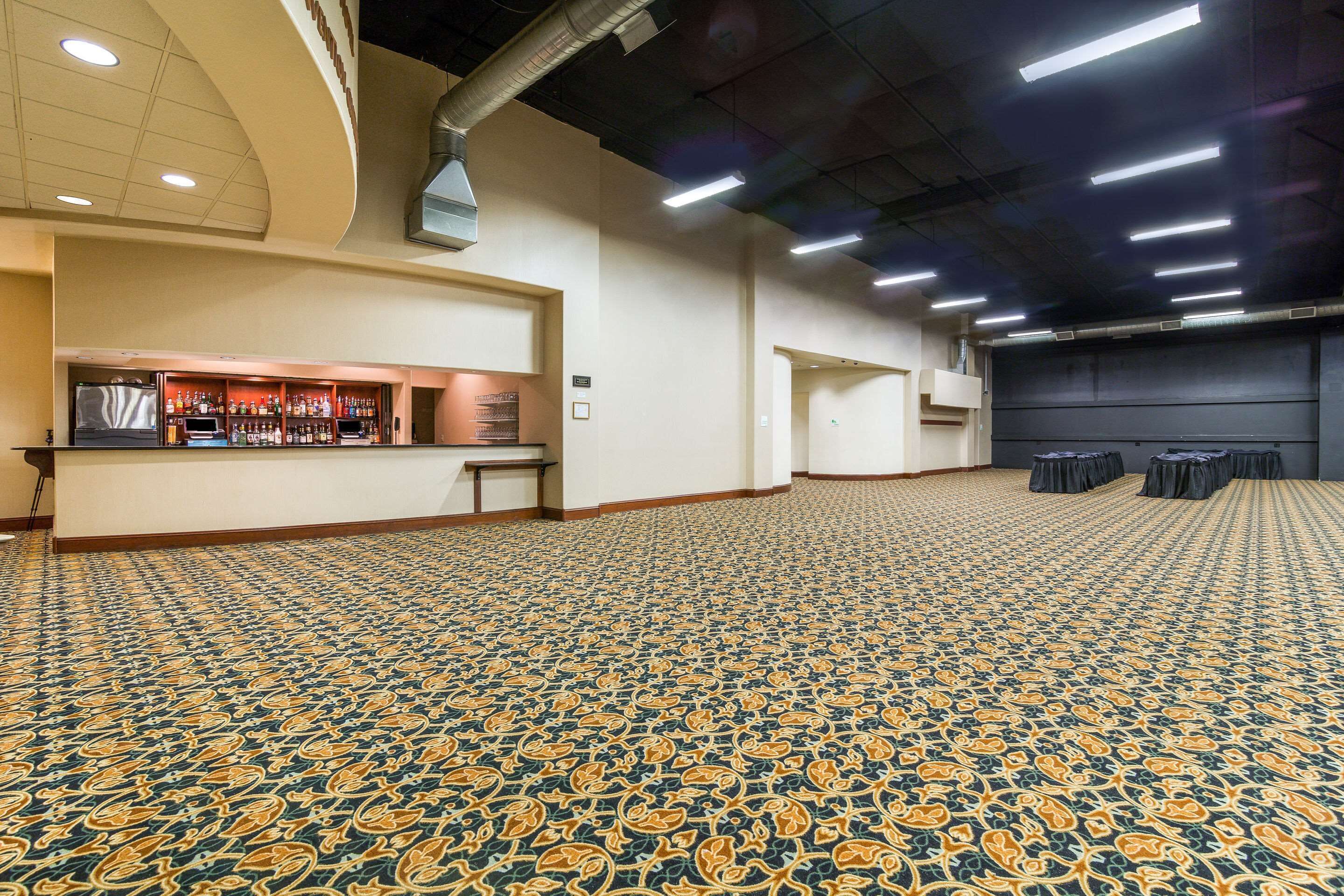 A spacious hall with patterned carpet, a bar area, and a stage.