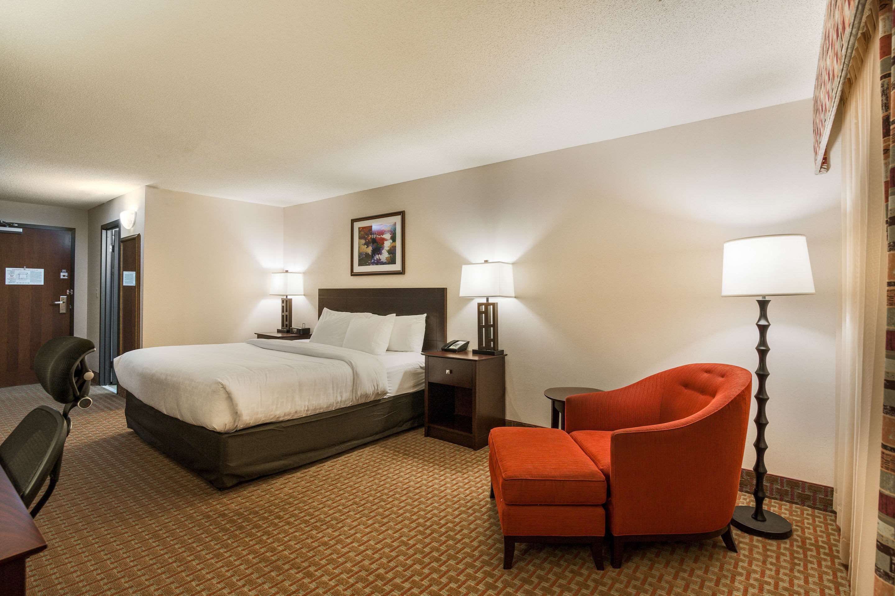 A hotel room with a bed, two bedside tables with lamps, a chair, and a desk.