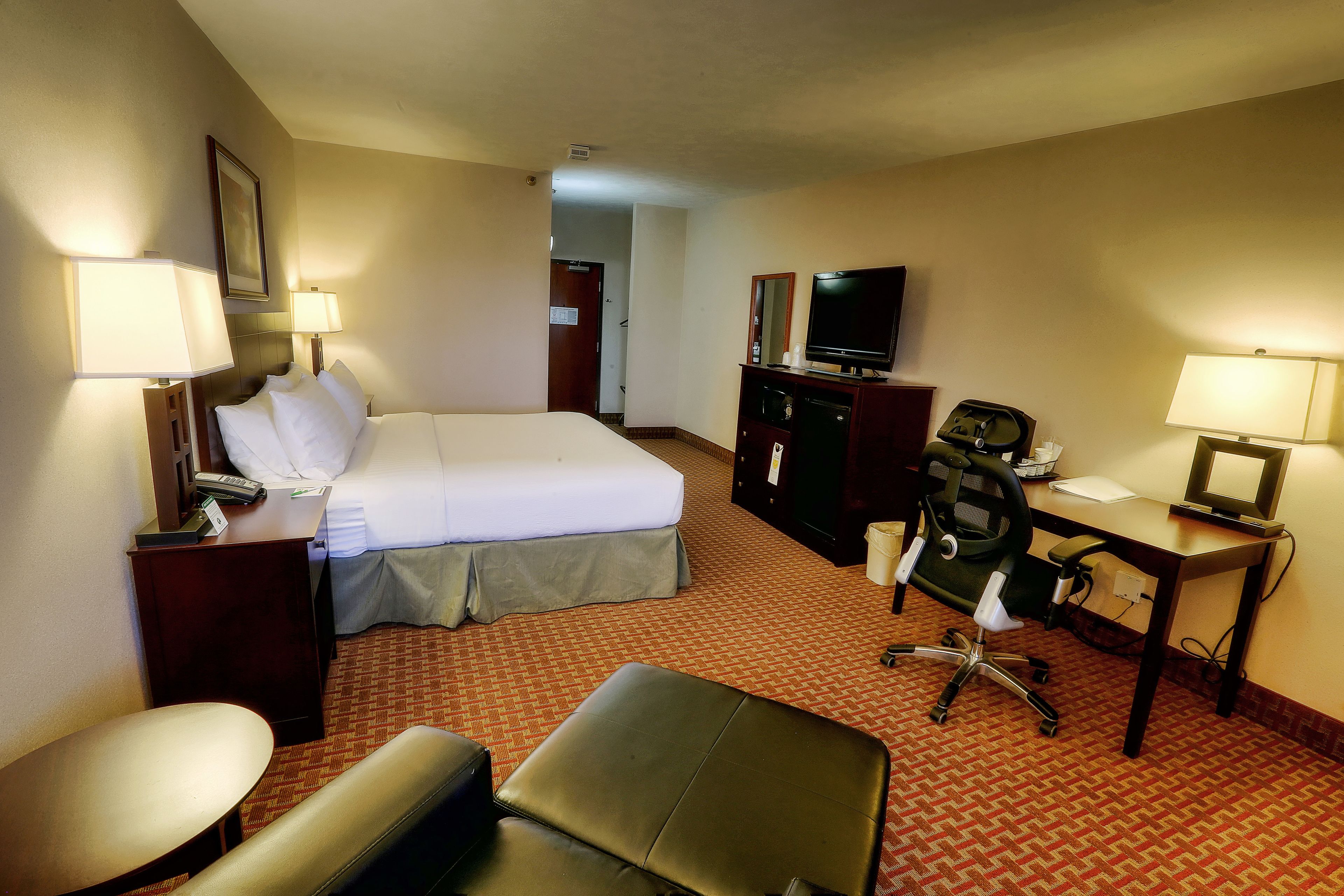 A hotel room with a bed, desk, chair, and a television.