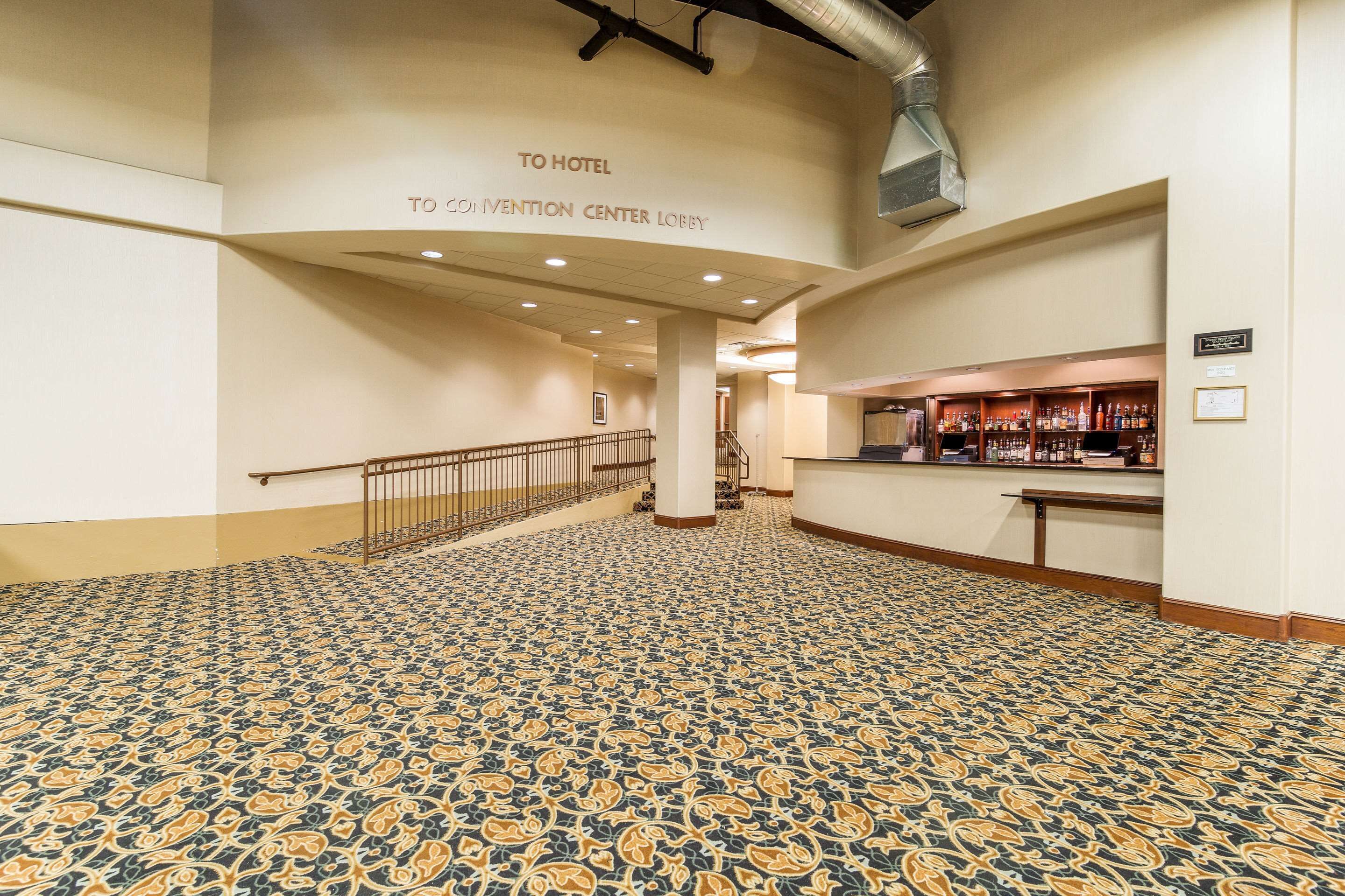 A spacious lobby with patterned carpet, a staircase, and a bar area.