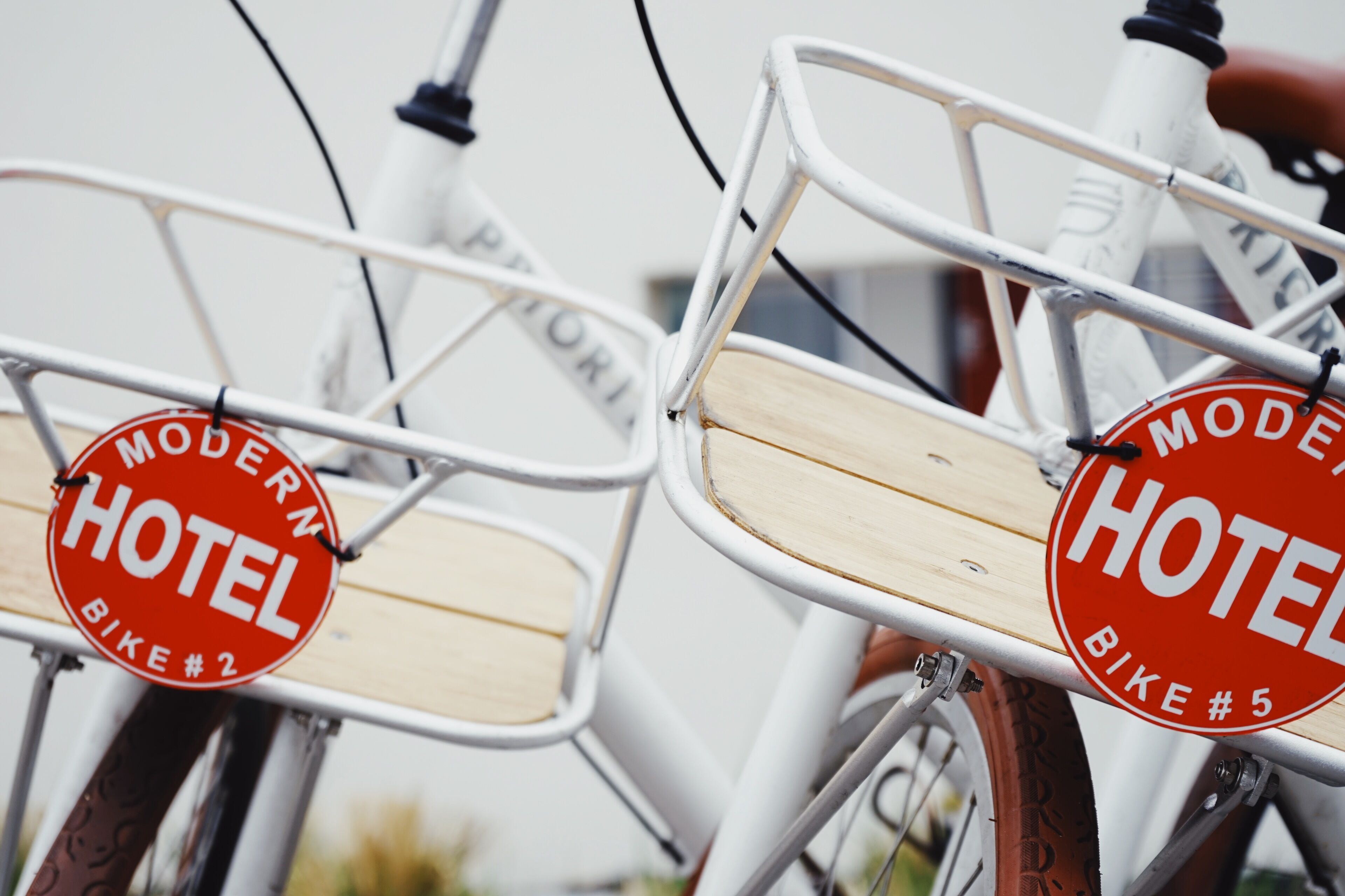 Two bicycles with wooden seats and metal frames, each with a red circular sign that reads "MODERN HOTEL BIKE #2" and "BIKE #5".