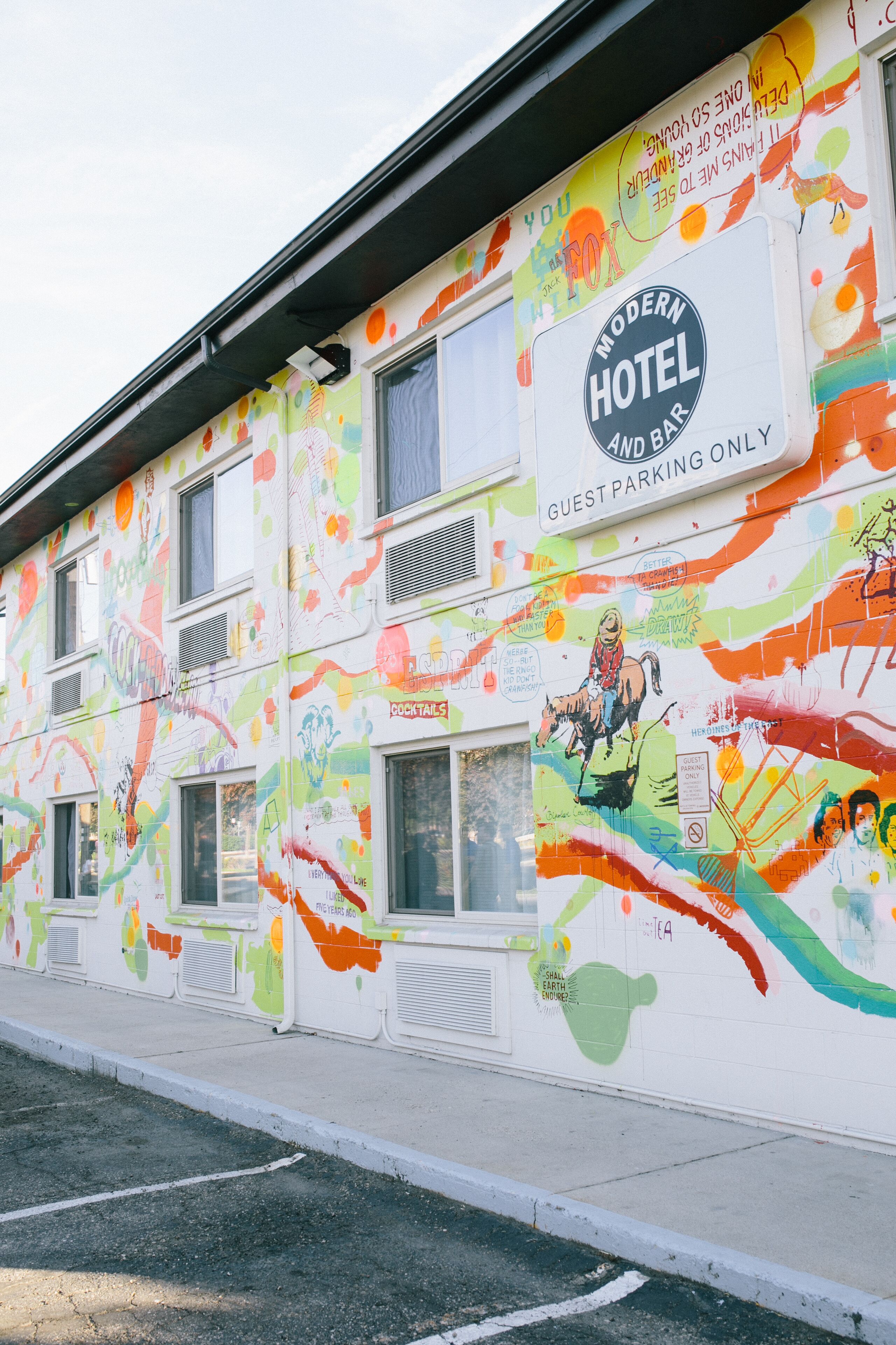 Un bâtiment aux couleurs vives, avec une enseigne indiquant un hôtel et un bar modernes, et proposant un parking pour les clients.